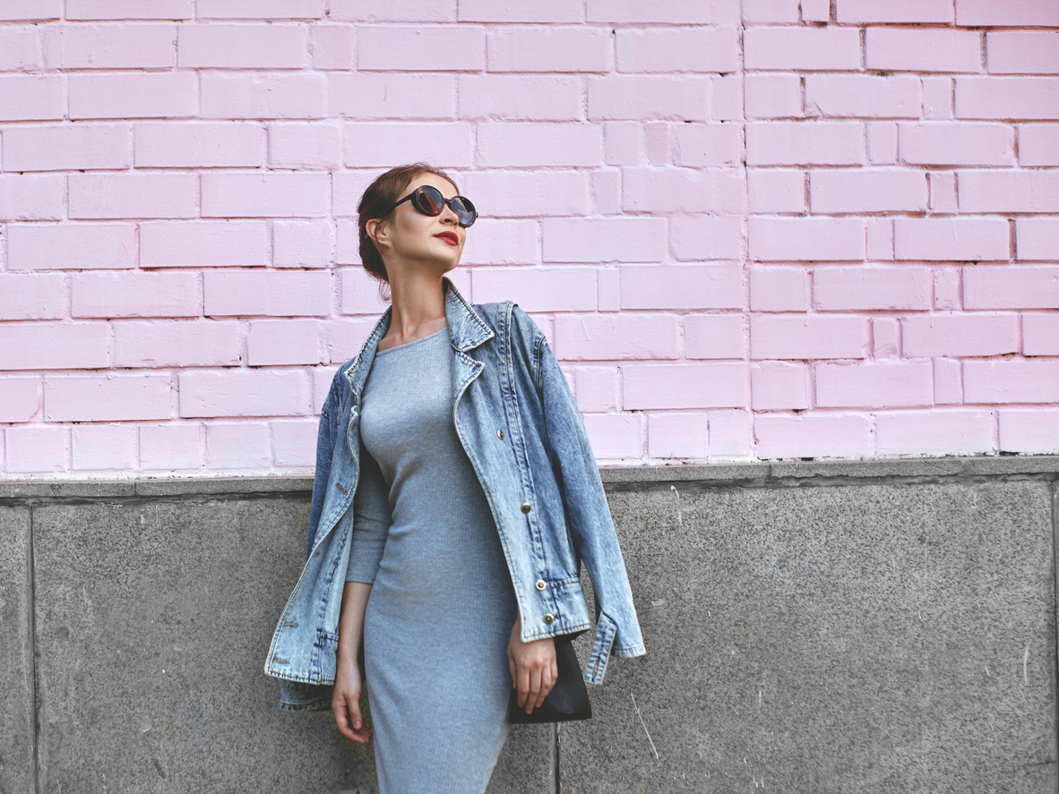 a girl wearing a grey casual dress, jeans jacket, posing on a pink wall