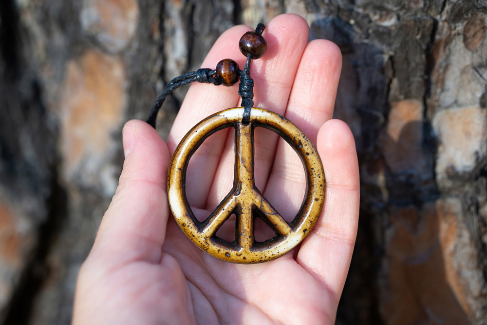 Handmade wooden peace sign necklace in hand against a tree trunk background, selective focus. No war concept