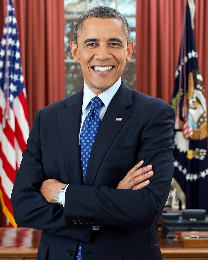 Obama standing with his arms folded and smiling.