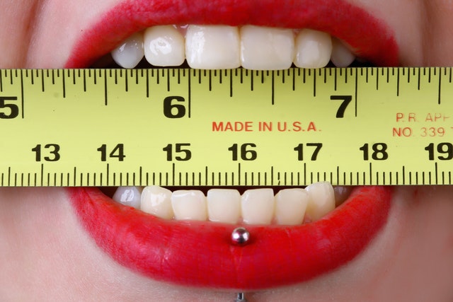  a close up of a mouth with a lip piercing a biting a tape measure