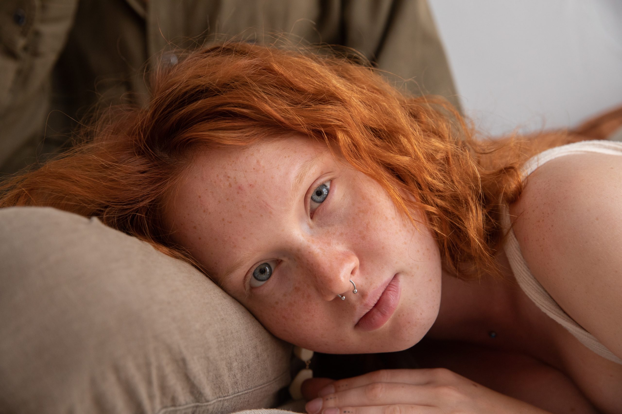 a redhead with septum piercings lying on someone’s lap