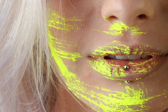 a woman with a lip piercing and yellow paint smeared on her face