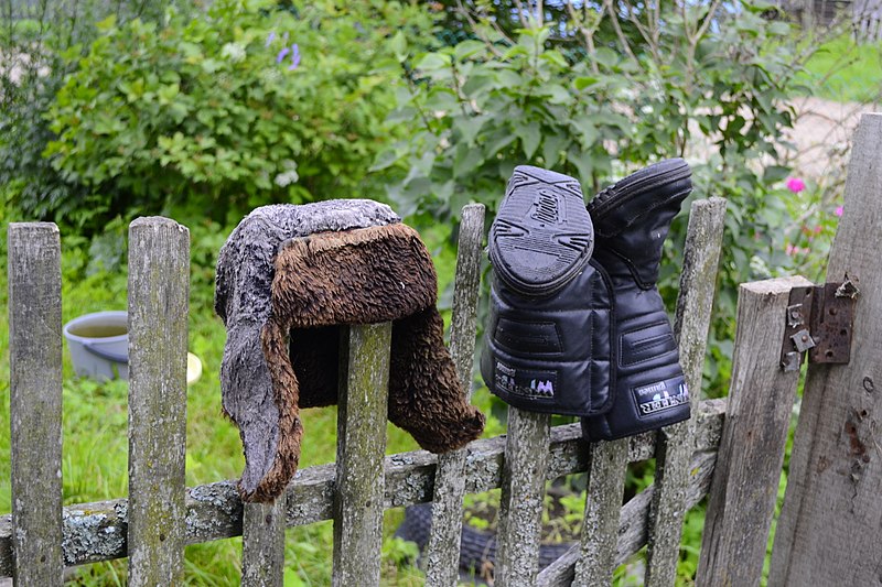 an Ushanka and boots hanged on a wooden fence