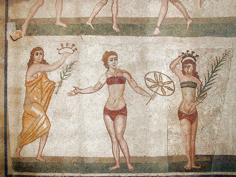 the detail of a mosaic featuring a woman with a palm of victory and wreath and a non-bikini-clad woman rushing in with a wreath and palm-leaf to crown another victor (in an athletic competition)