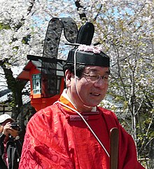 an old man smiling, wearing a red kimono and a Japanese traditional hat (kanmuri)