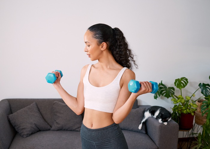 A serious young woman lifts small weights to get strong at home