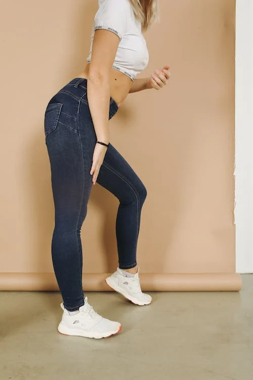 crop unrecognizable woman in jeans leaning forward on beige background
