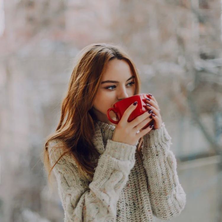 selective focus photography of a woman holding a red ceramic cup