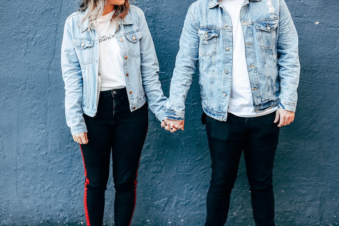 two people standing and holding their hands beside the blue wall