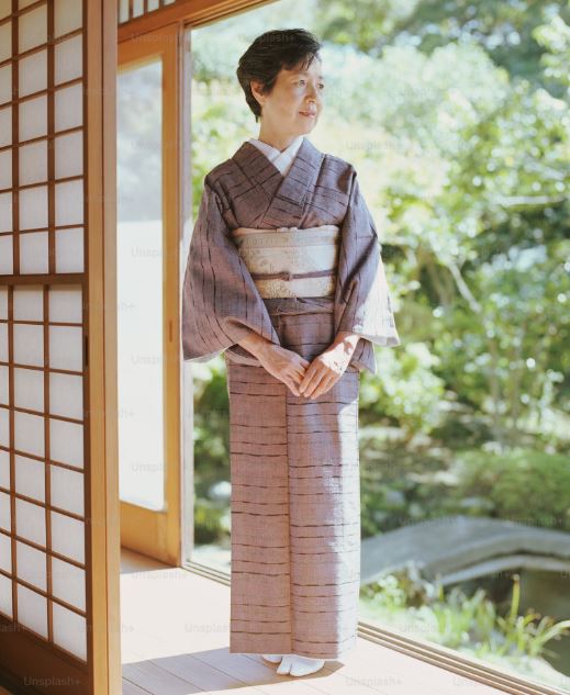 Senior woman in kimono standing in open doorway, looking away 