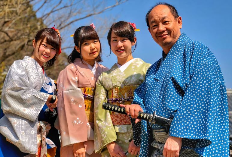 Three women wearing kimono beside man holding katana sword