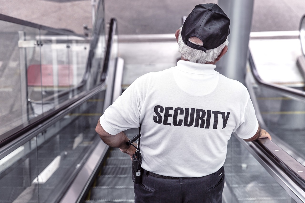the back of a security guard wearing a uniform and going down an escalator