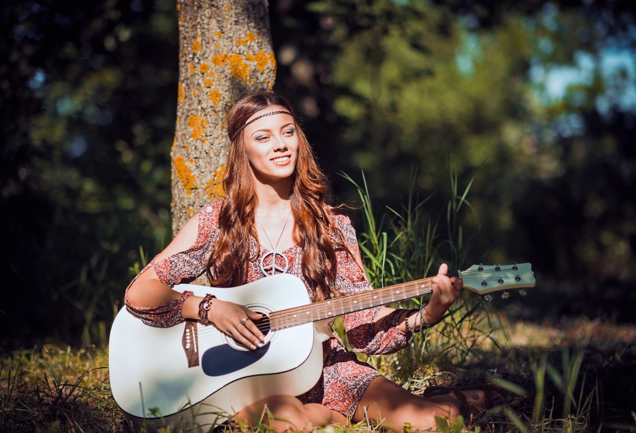 hippie girl sitting under tree and playing guitar wearing a peace symbol